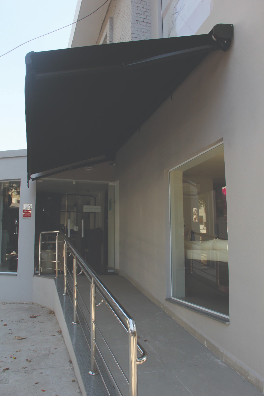 Toldo articulado preto instalado sobre acesso comercial